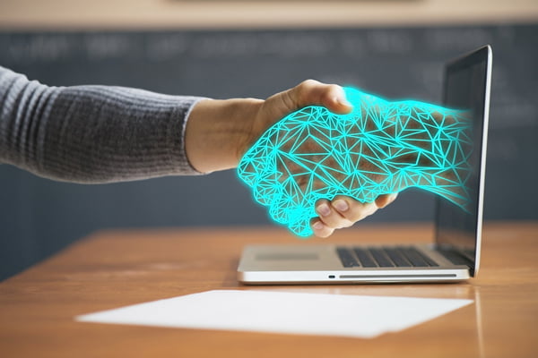 Two hands shaking through a computer representing holistic service models meeting digitalisation
