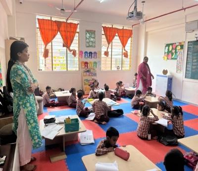 Active learning session at Lotus Petal Senior Secondary School Pupils in school uniform take part in academic activities in a classroom, supervised by two female teachers. The children sit on mats on the floor, concentrating on their schoolwork.