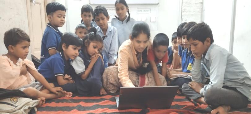 A group of attentive children, accompanied by a teacher, sitting in a circle on a carpet, explore together the contents of a laptop in a classroom in an inclusive school.